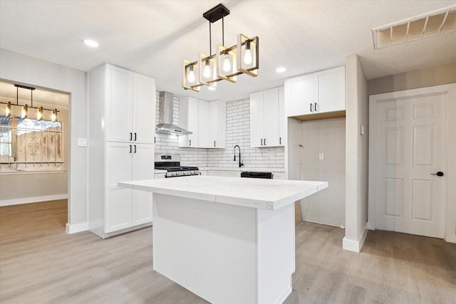 kitchen featuring gas stove, white cabinetry, wall chimney exhaust hood, decorative light fixtures, and a kitchen island