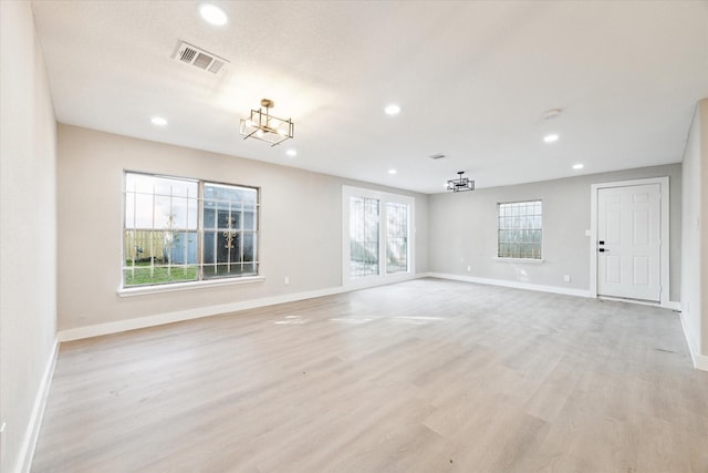 spare room featuring a notable chandelier, plenty of natural light, and light wood-type flooring