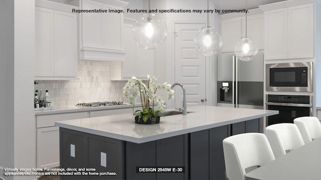 kitchen featuring sink, hanging light fixtures, stainless steel appliances, an island with sink, and white cabinets