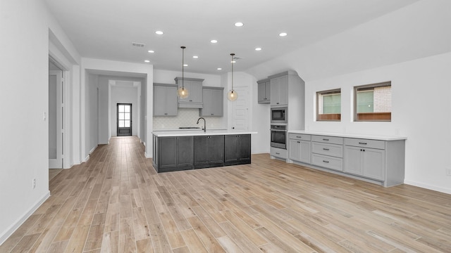 kitchen with tasteful backsplash, light wood-style flooring, appliances with stainless steel finishes, light countertops, and gray cabinetry