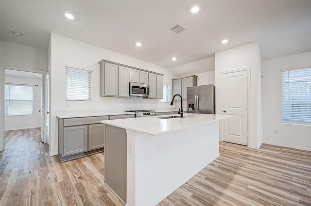 kitchen with gray cabinetry, a center island with sink, sink, light hardwood / wood-style flooring, and stainless steel appliances