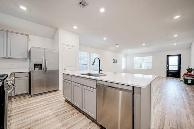 kitchen featuring gray cabinetry, sink, light hardwood / wood-style floors, a center island with sink, and appliances with stainless steel finishes