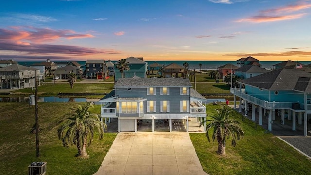 back house at dusk featuring a carport, a balcony, and a water view