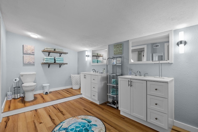 bathroom with wood-type flooring, vanity, toilet, and lofted ceiling