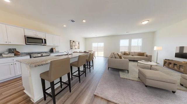 kitchen with white cabinets, a breakfast bar, stainless steel appliances, and a center island with sink