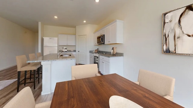 kitchen featuring a kitchen bar, stainless steel appliances, sink, white cabinetry, and an island with sink