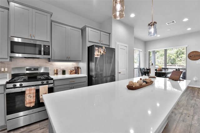 kitchen with appliances with stainless steel finishes, decorative light fixtures, tasteful backsplash, and gray cabinetry