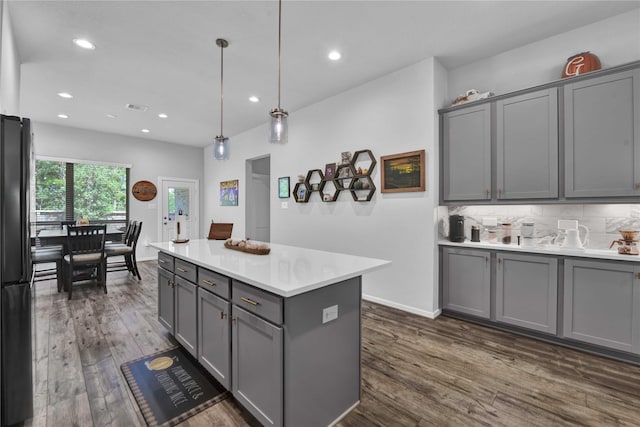 kitchen with gray cabinetry, a center island, hanging light fixtures, dark hardwood / wood-style floors, and backsplash