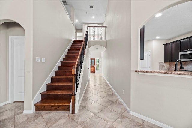 staircase with sink, a towering ceiling, and tile patterned floors