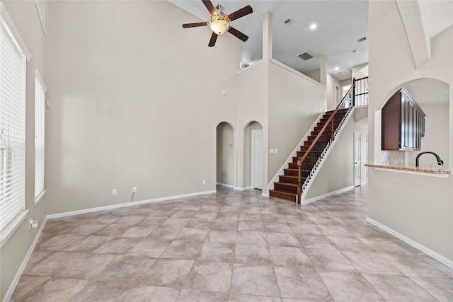 unfurnished living room featuring ceiling fan, plenty of natural light, and a high ceiling