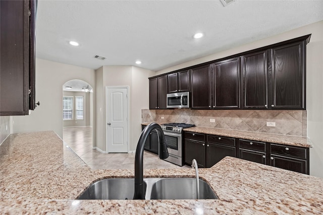 kitchen with light tile patterned flooring, appliances with stainless steel finishes, tasteful backsplash, sink, and dark brown cabinetry