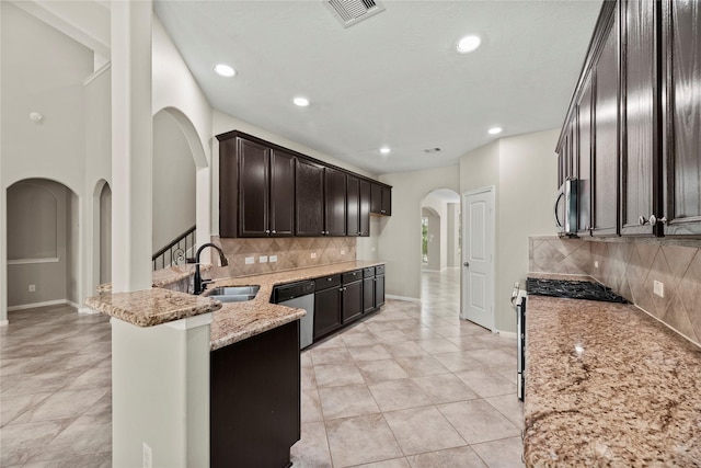 kitchen featuring sink, dark brown cabinets, kitchen peninsula, stainless steel appliances, and light stone countertops