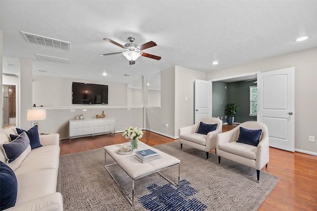 living room with wood-type flooring, ceiling fan, and a textured ceiling