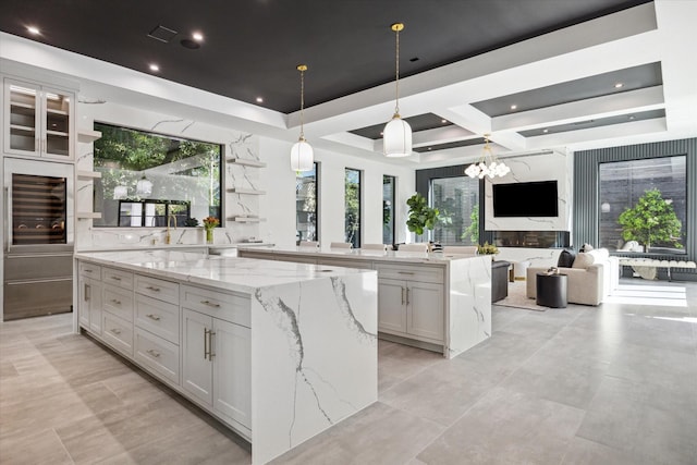 kitchen featuring decorative light fixtures, a large island, a notable chandelier, light stone counters, and white cabinetry