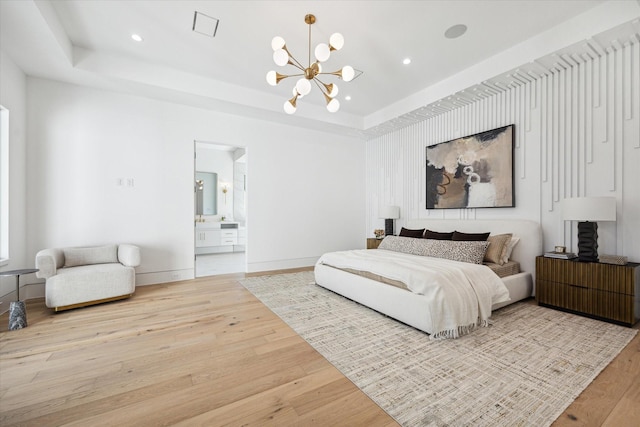 bedroom with a notable chandelier, light hardwood / wood-style floors, a raised ceiling, and ensuite bath