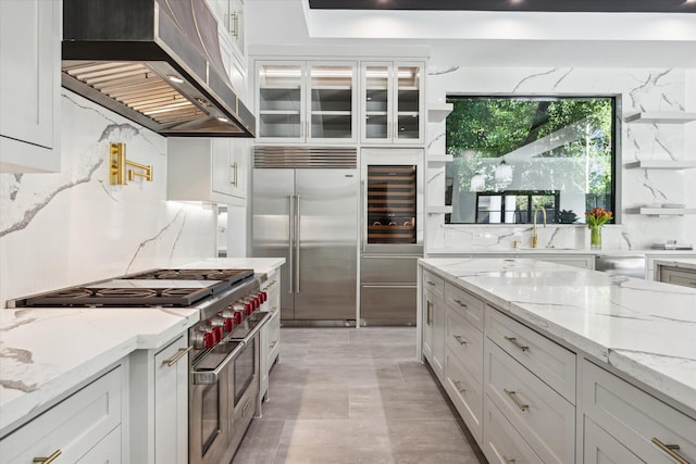 kitchen featuring ventilation hood, white cabinetry, high end appliances, and light stone counters