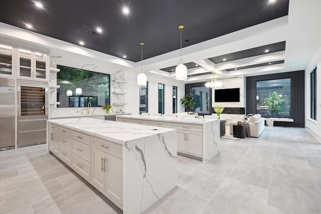 kitchen featuring a raised ceiling, white cabinetry, a spacious island, and light stone counters