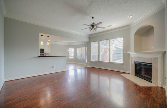 unfurnished living room featuring crown molding, hardwood / wood-style floors, a textured ceiling, a fireplace, and ceiling fan with notable chandelier