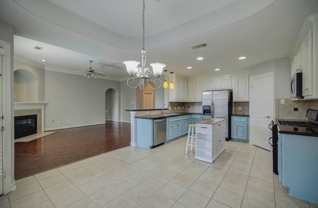 kitchen featuring white cabinetry, stainless steel appliances, kitchen peninsula, decorative light fixtures, and ceiling fan with notable chandelier