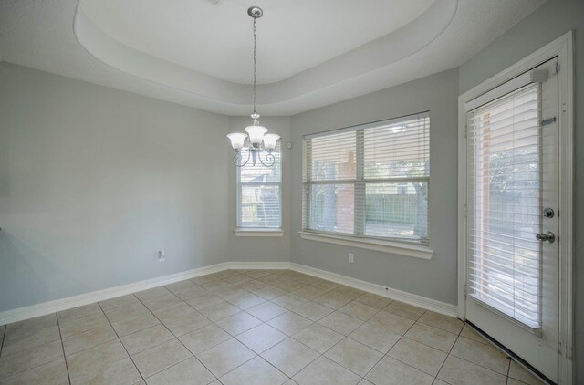 unfurnished room featuring a notable chandelier, light tile patterned flooring, a raised ceiling, and a healthy amount of sunlight