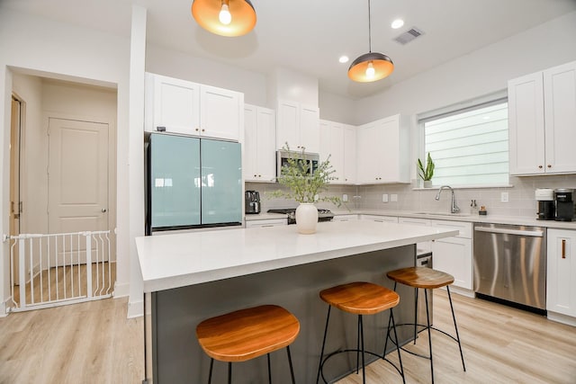 kitchen with a center island, sink, appliances with stainless steel finishes, decorative light fixtures, and white cabinetry