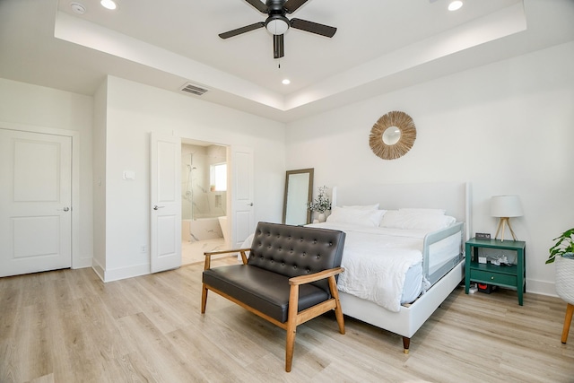 bedroom with ceiling fan, a raised ceiling, ensuite bathroom, and light hardwood / wood-style flooring