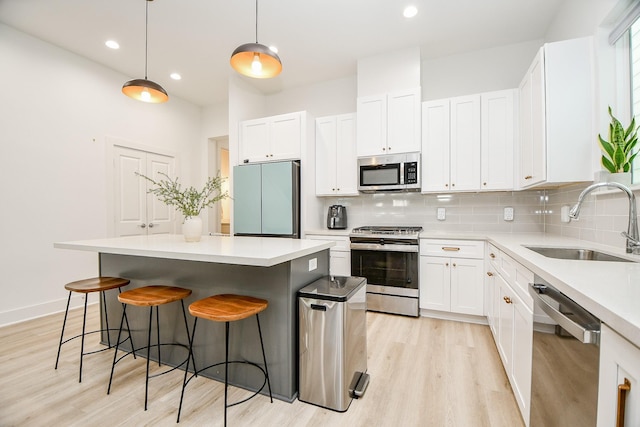 kitchen with sink, hanging light fixtures, a kitchen island, white cabinets, and appliances with stainless steel finishes