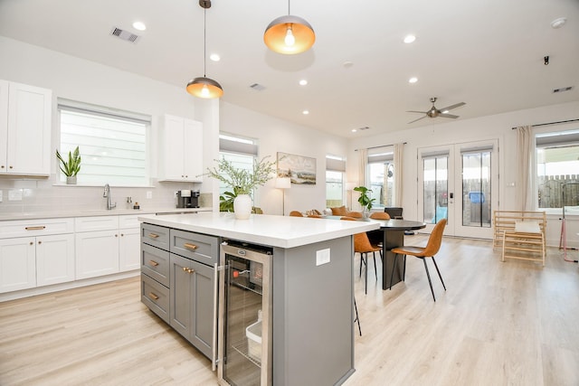 kitchen featuring pendant lighting, gray cabinetry, a center island, white cabinets, and wine cooler