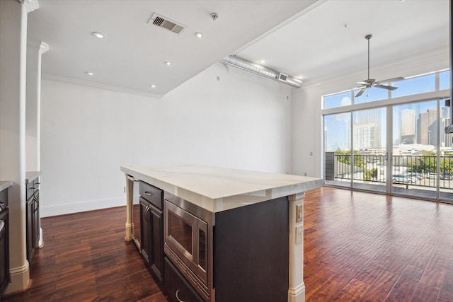 kitchen featuring dark brown cabinets, dark hardwood / wood-style flooring, a kitchen island, and stainless steel microwave