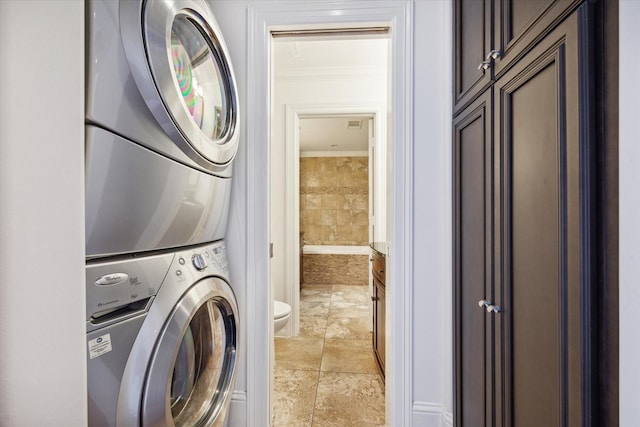 clothes washing area featuring cabinets, stacked washing maching and dryer, and ornamental molding