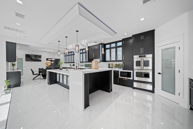 kitchen featuring sink, a kitchen breakfast bar, double oven, an island with sink, and pendant lighting