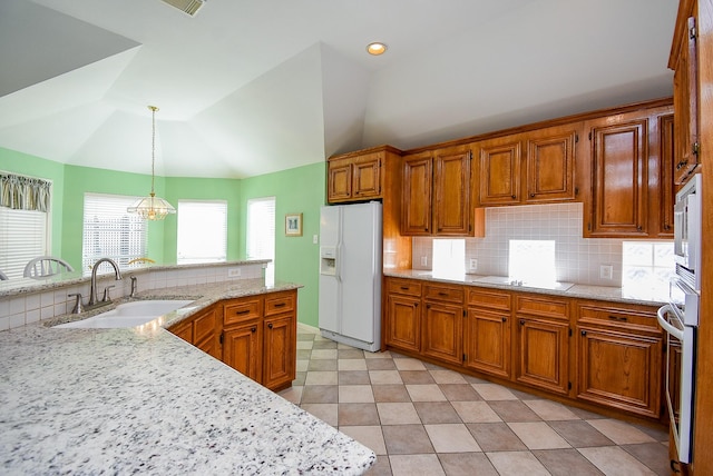 kitchen with white refrigerator with ice dispenser, sink, hanging light fixtures, oven, and vaulted ceiling