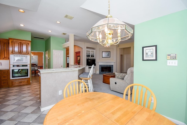 tiled dining area with a tile fireplace, lofted ceiling, and an inviting chandelier