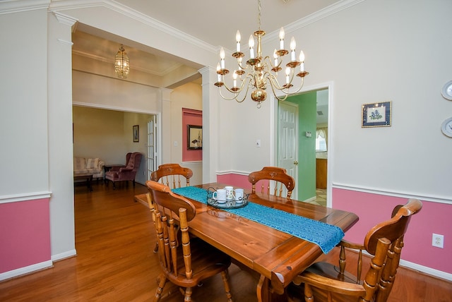 dining area with ornate columns, hardwood / wood-style flooring, crown molding, and a notable chandelier