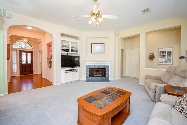 carpeted living room with a tile fireplace, built in features, decorative columns, and ceiling fan