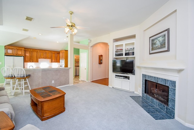 living room with built in shelves, a tile fireplace, carpet, and ceiling fan