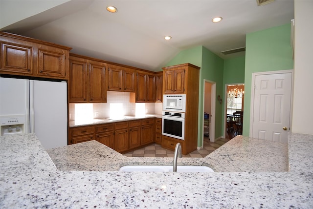 kitchen with white appliances, lofted ceiling, sink, a notable chandelier, and light stone counters