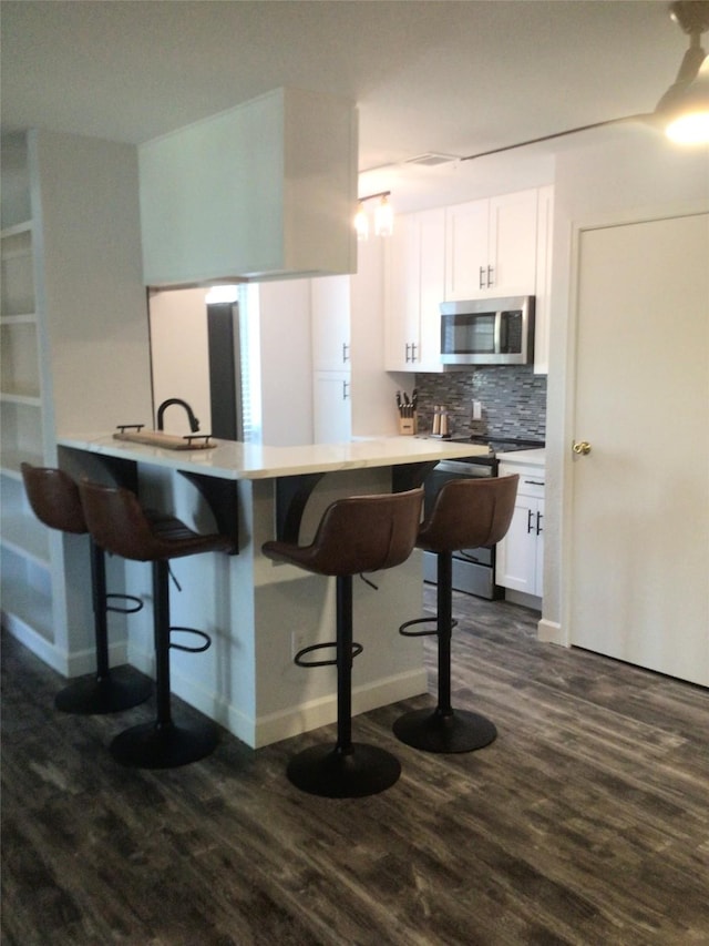 kitchen with a kitchen bar, dark hardwood / wood-style flooring, white cabinetry, and kitchen peninsula