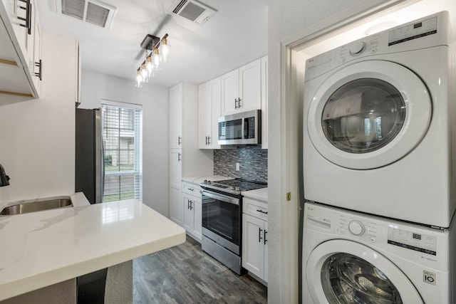 laundry area with dark wood-type flooring, stacked washer and dryer, visible vents, and a sink