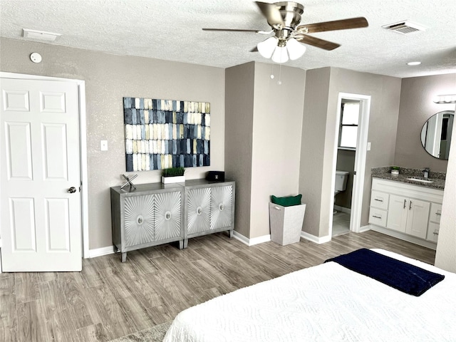 bedroom featuring ensuite bathroom, ceiling fan, light wood-type flooring, and a textured ceiling