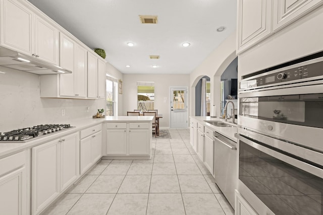 kitchen featuring kitchen peninsula, stainless steel appliances, sink, light tile patterned floors, and white cabinetry