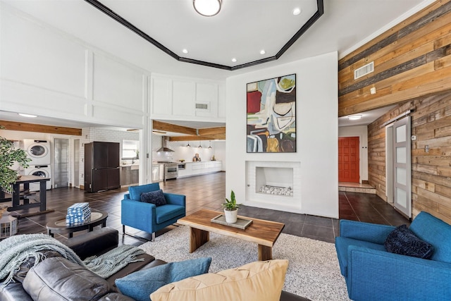 tiled living room featuring a barn door, ornamental molding, wooden walls, and stacked washer and clothes dryer