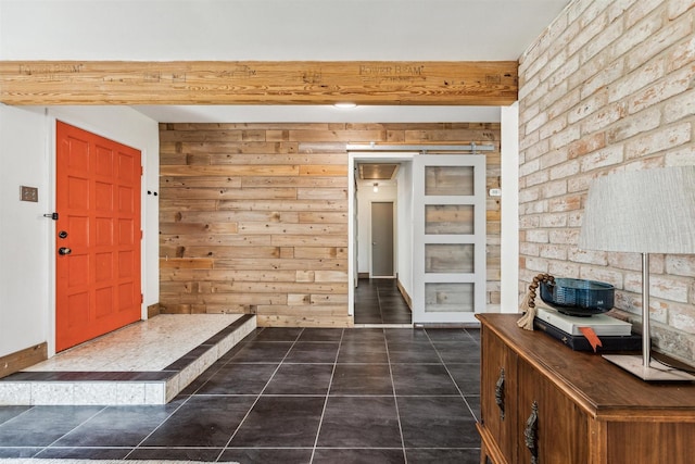 foyer entrance with beam ceiling, a barn door, dark tile patterned floors, and wood walls