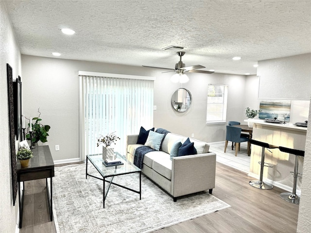 living room with ceiling fan, light hardwood / wood-style flooring, and a textured ceiling