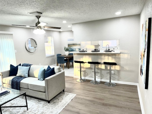 living room with ceiling fan, light hardwood / wood-style floors, and a textured ceiling