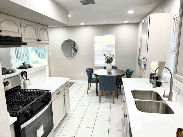 kitchen with sink, range hood, stainless steel range with gas stovetop, white cabinetry, and light tile patterned flooring