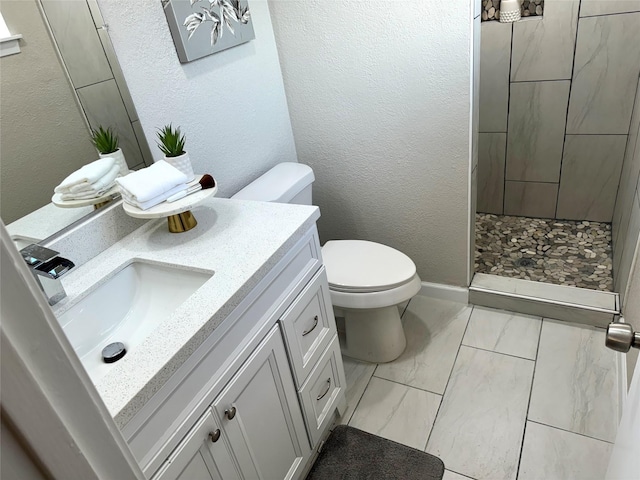 bathroom with a tile shower, vanity, and toilet