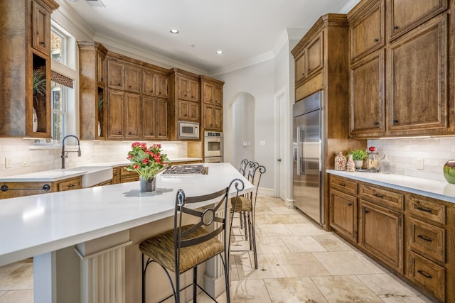 kitchen with a kitchen island, a breakfast bar, built in appliances, and decorative backsplash