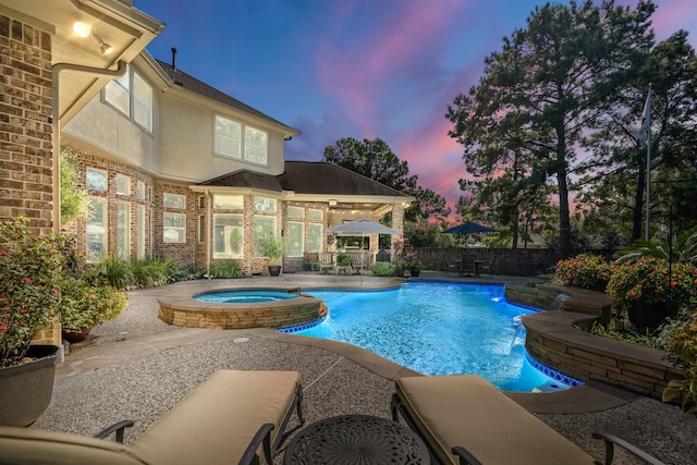 pool at dusk with an in ground hot tub and a patio area