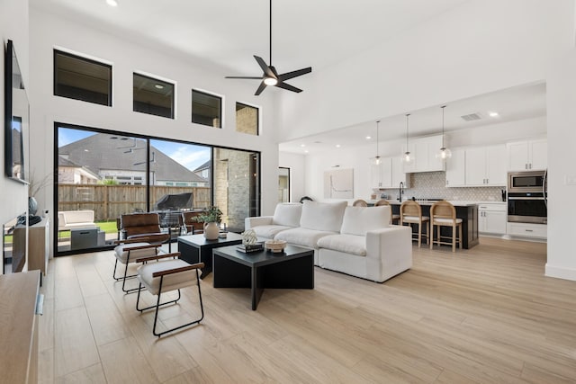 living room with ceiling fan, a towering ceiling, and light hardwood / wood-style flooring